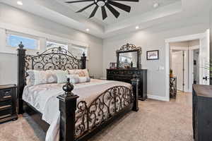 Carpeted bedroom featuring ceiling fan and a raised ceiling