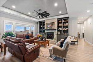 Living room featuring light hardwood / wood-style floors, built in shelves, a raised ceiling, and a fireplace