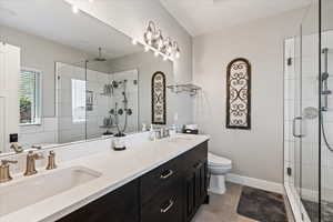 Bathroom featuring a shower with door, dual bowl vanity, tile flooring, and toilet