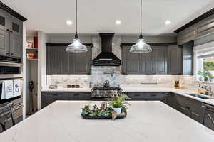 Kitchen featuring hanging light fixtures, stainless steel appliances, sink, tasteful backsplash, and custom exhaust hood