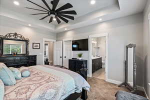 Carpeted bedroom with ensuite bathroom, ceiling fan, and a tray ceiling