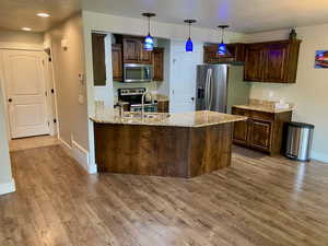 Kitchen featuring sink, dark brown cabinetry, light hardwood / wood-style flooring, light stone counters, and stainless steel appliances