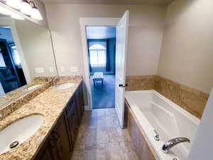 Bathroom featuring tiled bath, double sink vanity, and tile patterned flooring