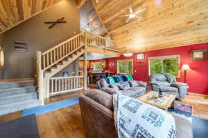 Living room with hardwood / wood-style floors, ceiling fan with notable chandelier, high vaulted ceiling, and wood ceiling