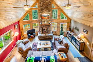 Living room featuring wood walls, wood-type flooring, ceiling fan, and high vaulted ceiling