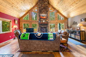 Living room with high vaulted ceiling, a fireplace, wooden ceiling, and wood-type flooring