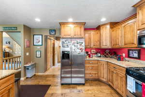 Kitchen with stainless steel appliances, light hardwood / wood-style floors, light stone countertops, and a textured ceiling