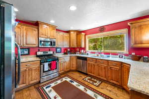 Kitchen featuring stainless steel appliances, sink, light stone countertops, a textured ceiling, and wood-type flooring