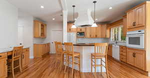 Kitchen with light wood-type flooring, white appliances, a kitchen island, a kitchen breakfast bar, and light stone countertops