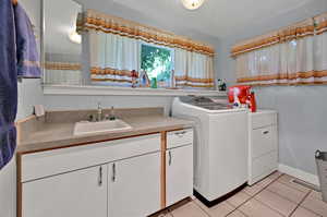 Laundry room with washer and clothes dryer, sink, cabinets, a textured ceiling, and light tile patterned floors