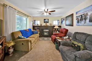 Living room with a fireplace, carpet, ceiling fan, and a wealth of natural light