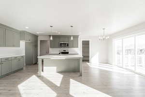 Kitchen with a center island with sink, stainless steel appliances, hanging light fixtures, and light hardwood / wood-style floors