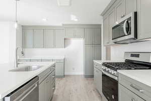 Kitchen with appliances with stainless steel finishes, gray cabinets, hanging light fixtures, sink, and light hardwood / wood-style floors