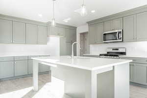 Kitchen with stainless steel appliances, light wood-type flooring, decorative light fixtures, sink, and an island with sink