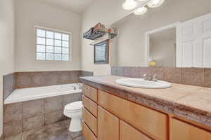 Primary Bathroom with tile floors, large vanity, tiled bath, and toilet