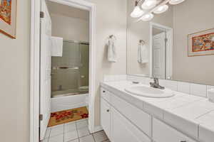 Full bathroom featuring tile floors, vanity with extensive cabinet space, bath / shower combo with glass door, and toilet