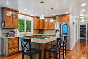 Kitchen with stainless steel appliances, sink, hanging light fixtures, decorative backsplash, and dark wood-type flooring