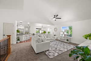 Living room with ceiling fan with notable chandelier, hardwood / wood-style floors, sink, and high vaulted ceiling