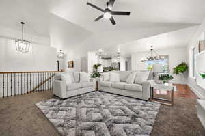 Carpeted living room with ceiling fan with notable chandelier and vaulted ceiling