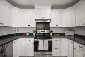 Kitchen featuring appliances with stainless steel finishes, white cabinetry, decorative backsplash, and wall chimney range hood