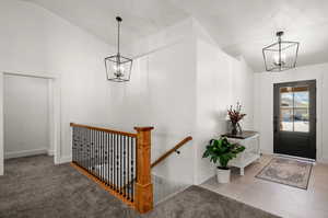 Carpeted entrance foyer featuring an inviting chandelier and lofted ceiling