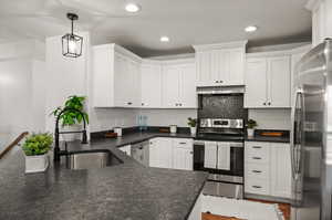 Kitchen with white cabinetry, tasteful backsplash, stainless steel appliances, wood-type flooring, and decorative light fixtures