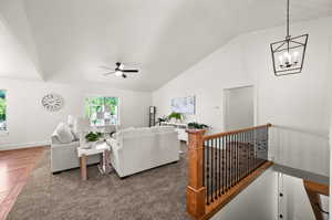 Living room with dark hardwood / wood-style floors, ceiling fan with notable chandelier, and lofted ceiling