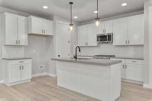 Kitchen featuring pendant lighting, white cabinets, a center island with sink, and stainless steel appliances