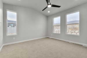 Carpeted spare room with plenty of natural light, ceiling fan, and lofted ceiling