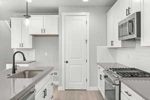 Kitchen featuring sink, white cabinetry, stainless steel appliances, and hanging light fixtures