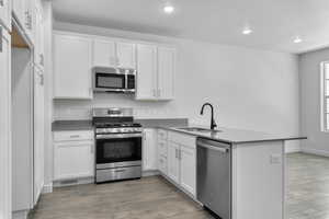 Kitchen featuring white cabinetry, hardwood / wood-style floors, sink, appliances with stainless steel finishes, and kitchen peninsula