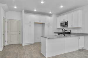 Kitchen with appliances with stainless steel finishes, kitchen peninsula, light hardwood / wood-style floors, and white cabinetry