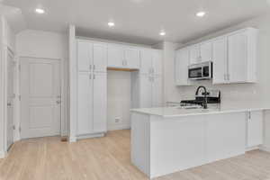 Kitchen with white cabinetry, kitchen peninsula, light wood-type flooring, and stainless steel appliances