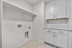 Washroom with cabinets, light tile patterned flooring, hookup for an electric dryer, and washer hookup