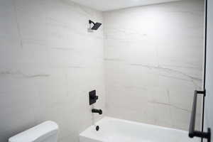 Bathroom featuring tiled shower / bath combo and toilet