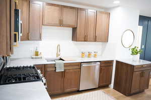 Kitchen featuring dishwasher, backsplash, light stone counters, and light wood-type flooring