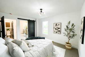 Bedroom featuring a barn door, ensuite bathroom, and carpet