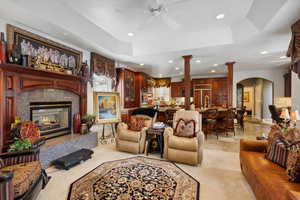 Carpeted living room with ceiling fan, a tray ceiling, sink, ornate columns, and a tile fireplace