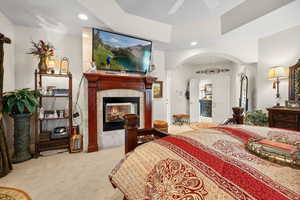 Carpeted bedroom with ensuite bathroom, a tiled fireplace, ceiling fan, and a raised ceiling