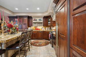 Kitchen featuring a breakfast bar area, light stone counters, light tile patterned floors, decorative backsplash, and stainless steel range with gas cooktop