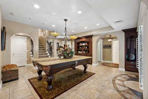 Game room with a tray ceiling, a notable chandelier, and light tile patterned floors