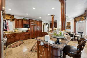 Kitchen with light tile patterned flooring, a breakfast bar, decorative columns, ceiling fan, and built in appliances