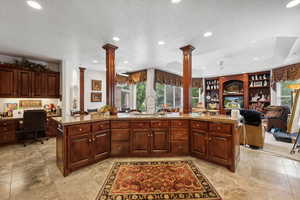 Kitchen featuring decorative columns, ceiling fan, a raised ceiling, and light stone countertops