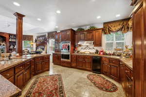 Kitchen with sink, appliances with stainless steel finishes, ornate columns, stone countertops, and light tile patterned floors