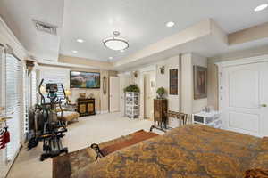 Bedroom with light carpet, a tray ceiling, and a textured ceiling