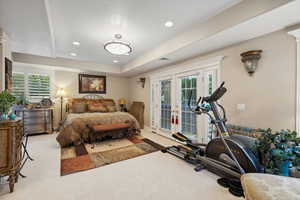 Carpeted bedroom with access to exterior, multiple windows, french doors, and a tray ceiling