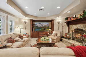 Carpeted living room featuring decorative columns, a fireplace, and a tray ceiling