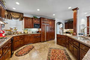 Kitchen featuring built in appliances, decorative columns, sink, light tile patterned floors, and light stone countertops