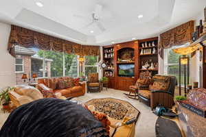 Carpeted living room with ceiling fan, built in shelves, and a tray ceiling