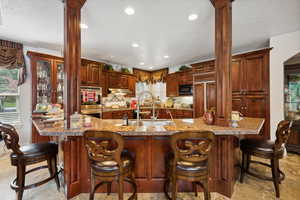 Kitchen with built in appliances, sink, light stone countertops, a breakfast bar, and light tile patterned floors